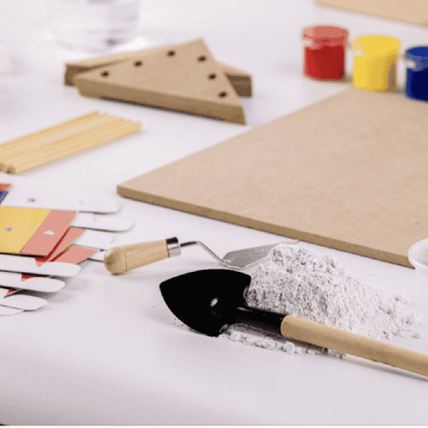 Children's play tools including a shovel and sand pail on a white surface with craft materials.