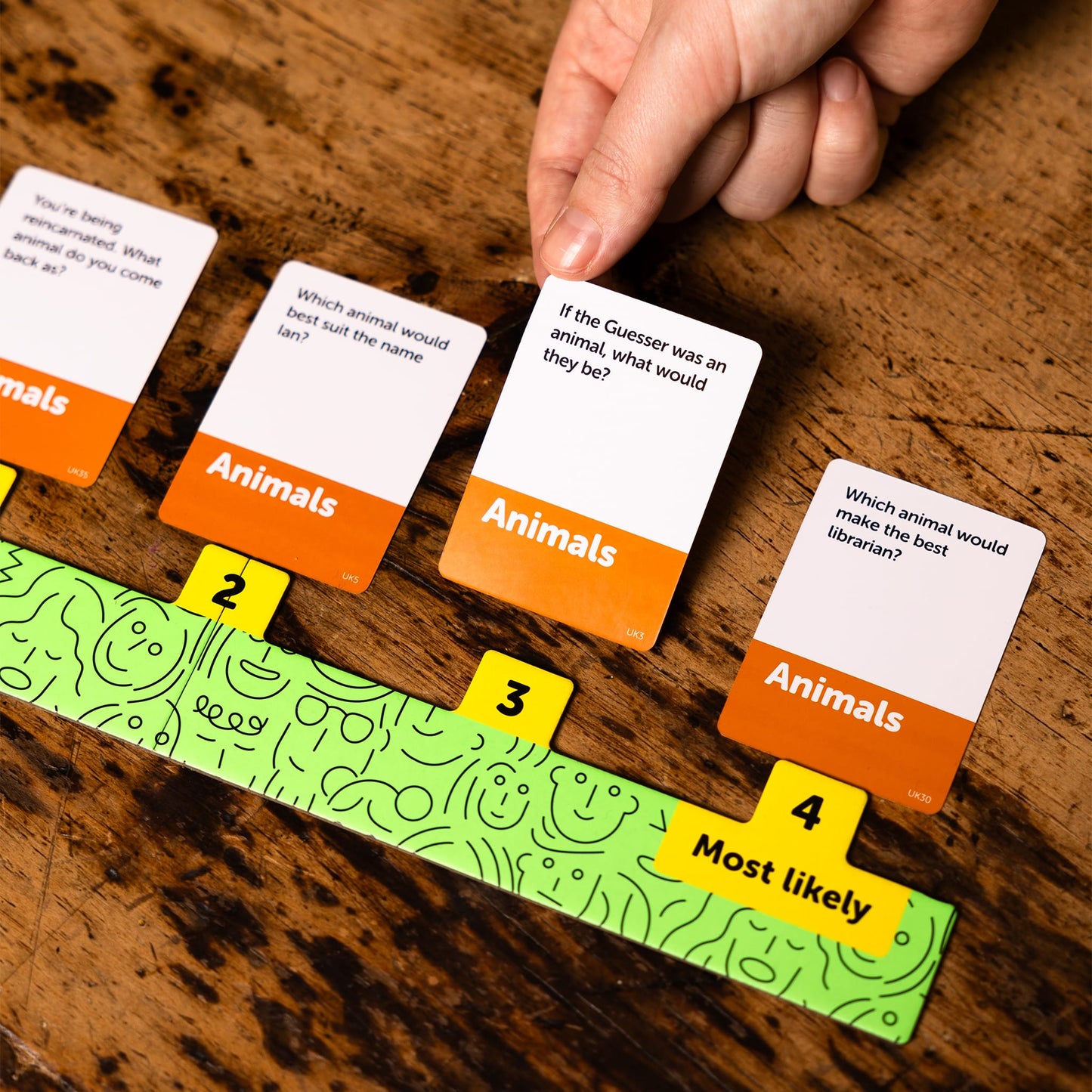 Dumb Questions To Ask Your Friends game with cards and a scoring track on a wooden surface