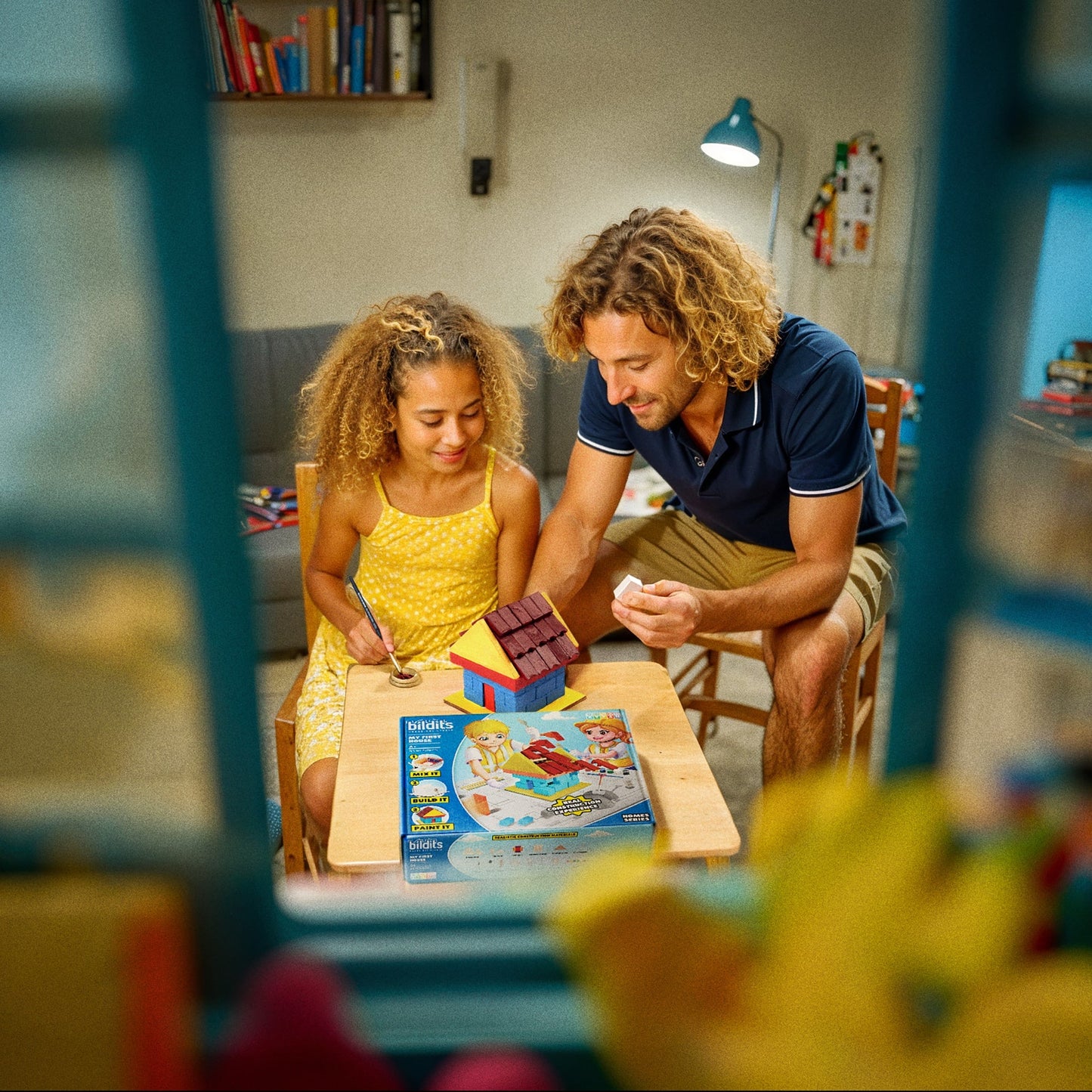 Dad and daughter playing building My First House at a table in a room.