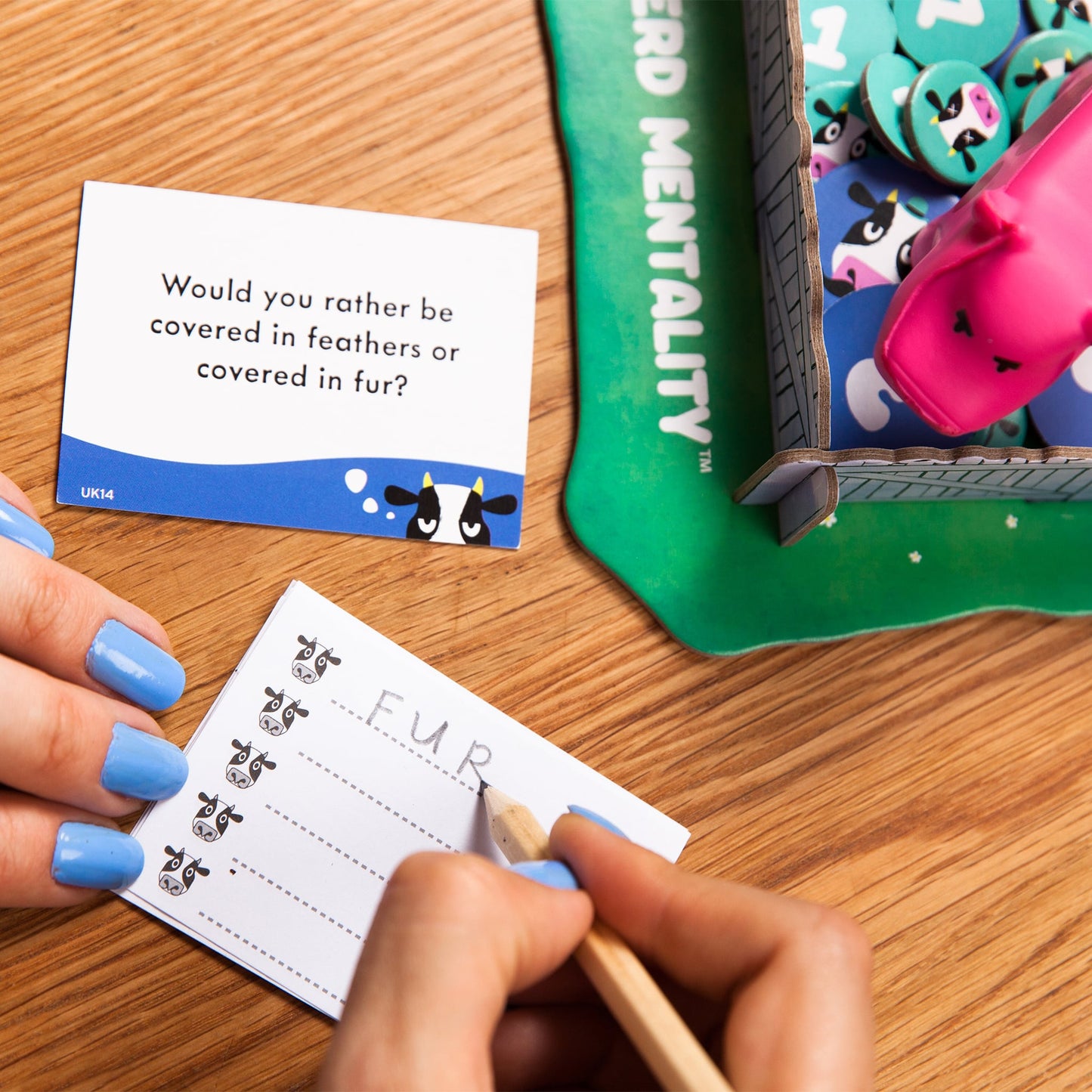 Person playing a card game with a question card and a scoring device on a wooden table.