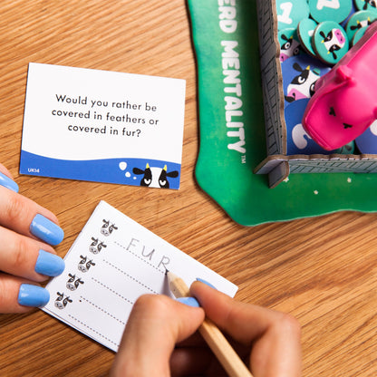 Person playing a card game with a question card and a scoring device on a wooden table.