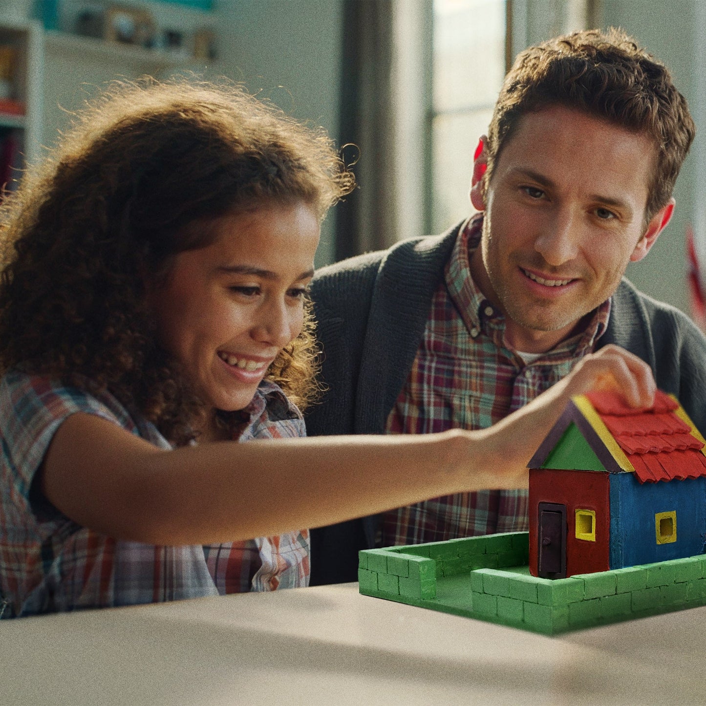 Man and young girl playing with a toy house in a room.