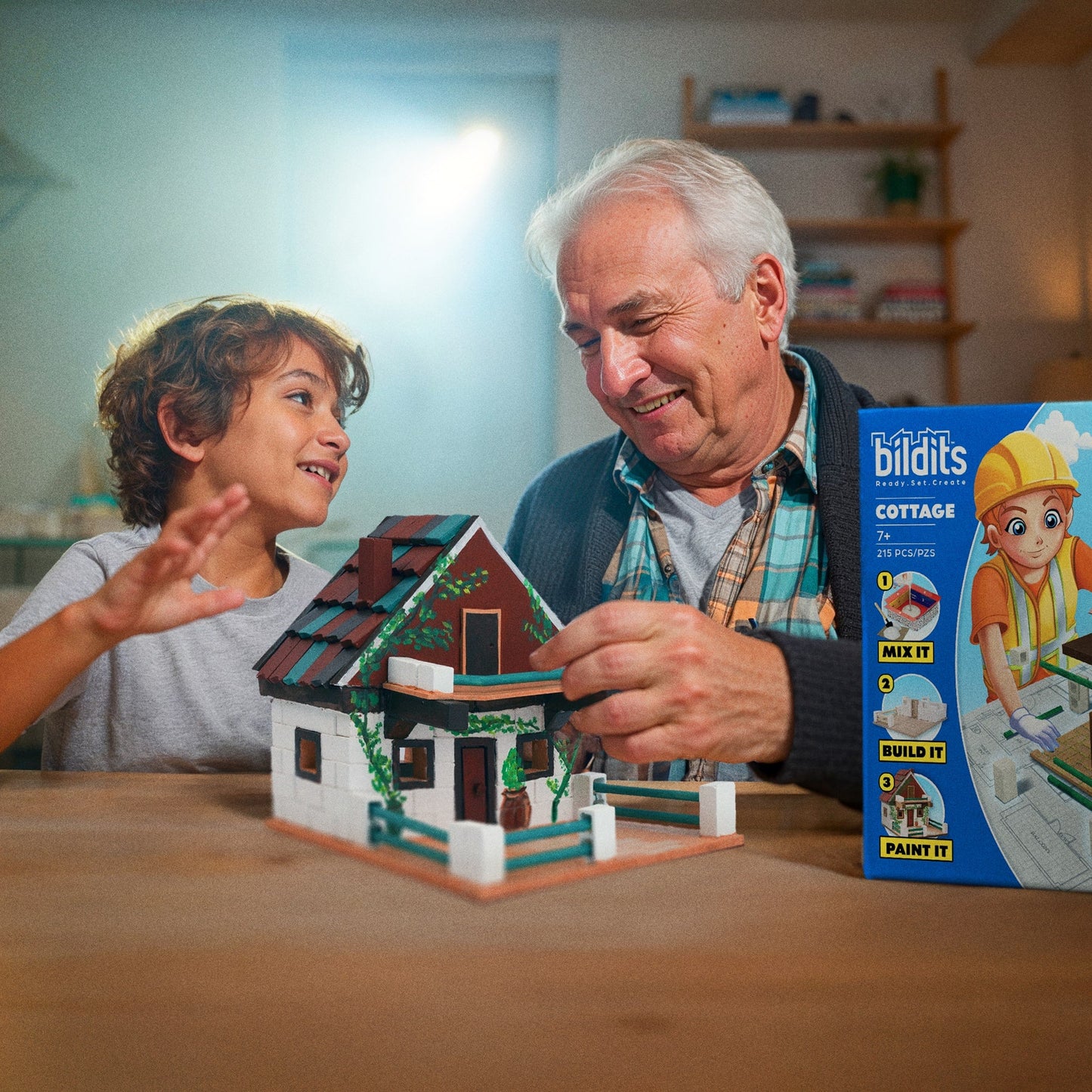 Man and child playing with a miniature house model, with a Biltits toy packaging in the background.