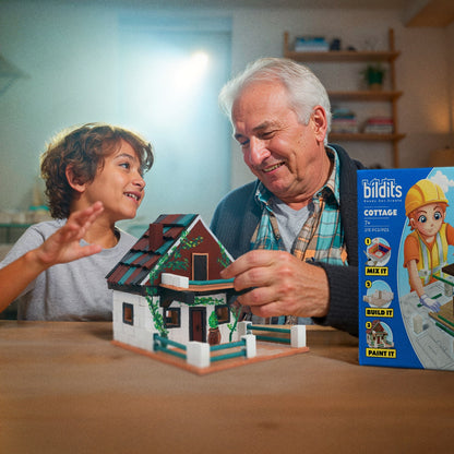 Man and child playing with a miniature house model, with a Biltits toy packaging in the background.