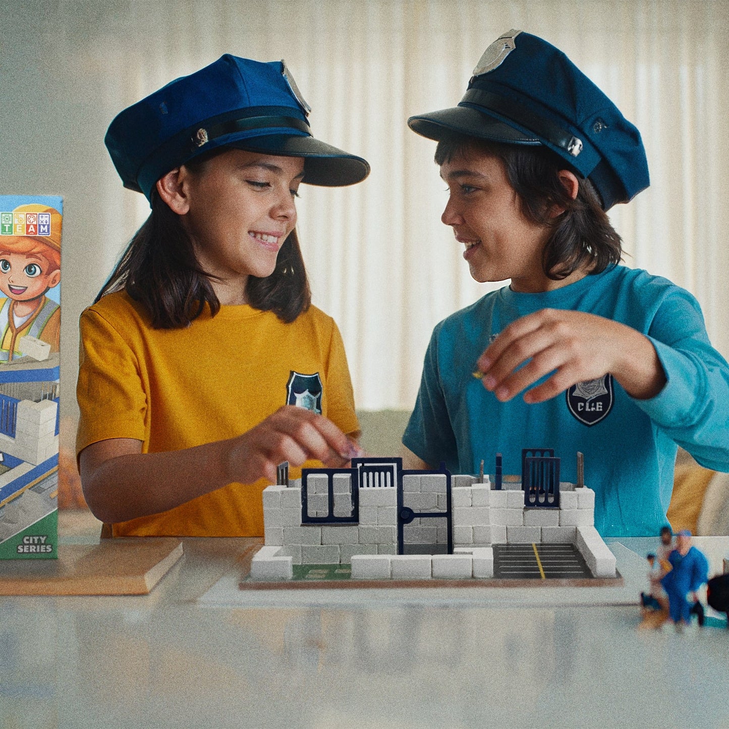 Two children playing with a toy city set, wearing blue hats.