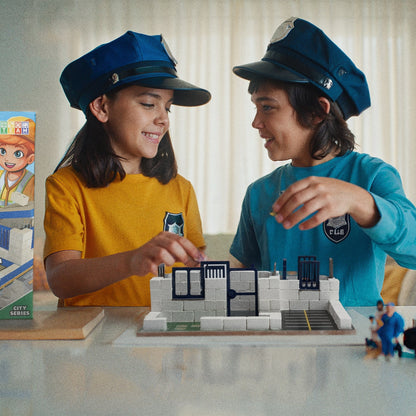Two children playing with a toy city set, wearing blue hats.
