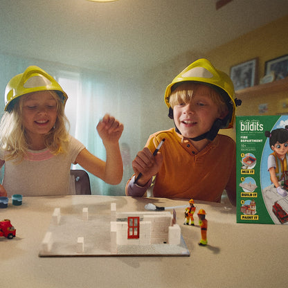 Two children playing with a toy building set and figurines, with a 'Buildits' toy box in the background.