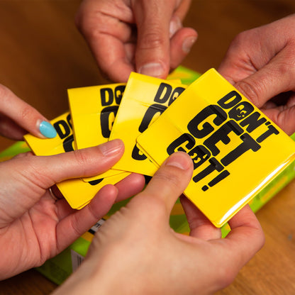 Hands holding yellow cards with 'Don't Get Got' text on a wooden surface