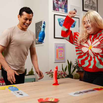 Two people playing Chicken vs Hotdog with colorful game pieces on a wooden table.